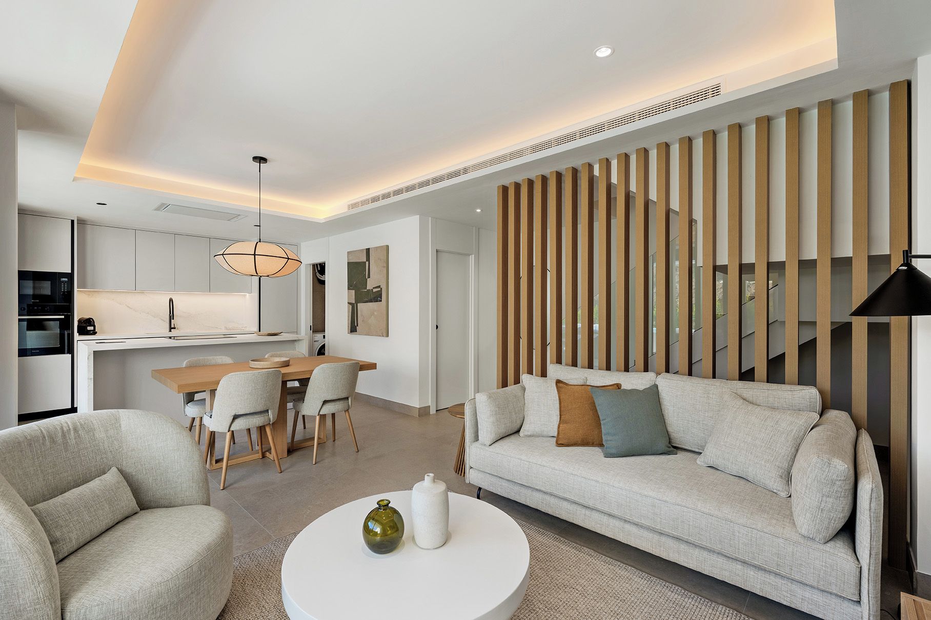 A modern living room with a sofa, chairs, a coffee table, and a kitchen area with a dining table and chairs.