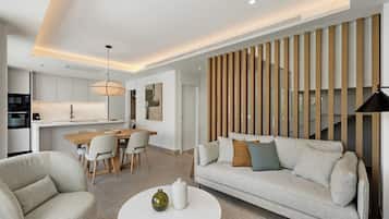 A modern living room with a sofa, chairs, a coffee table, and a kitchen area with a dining table and chairs.