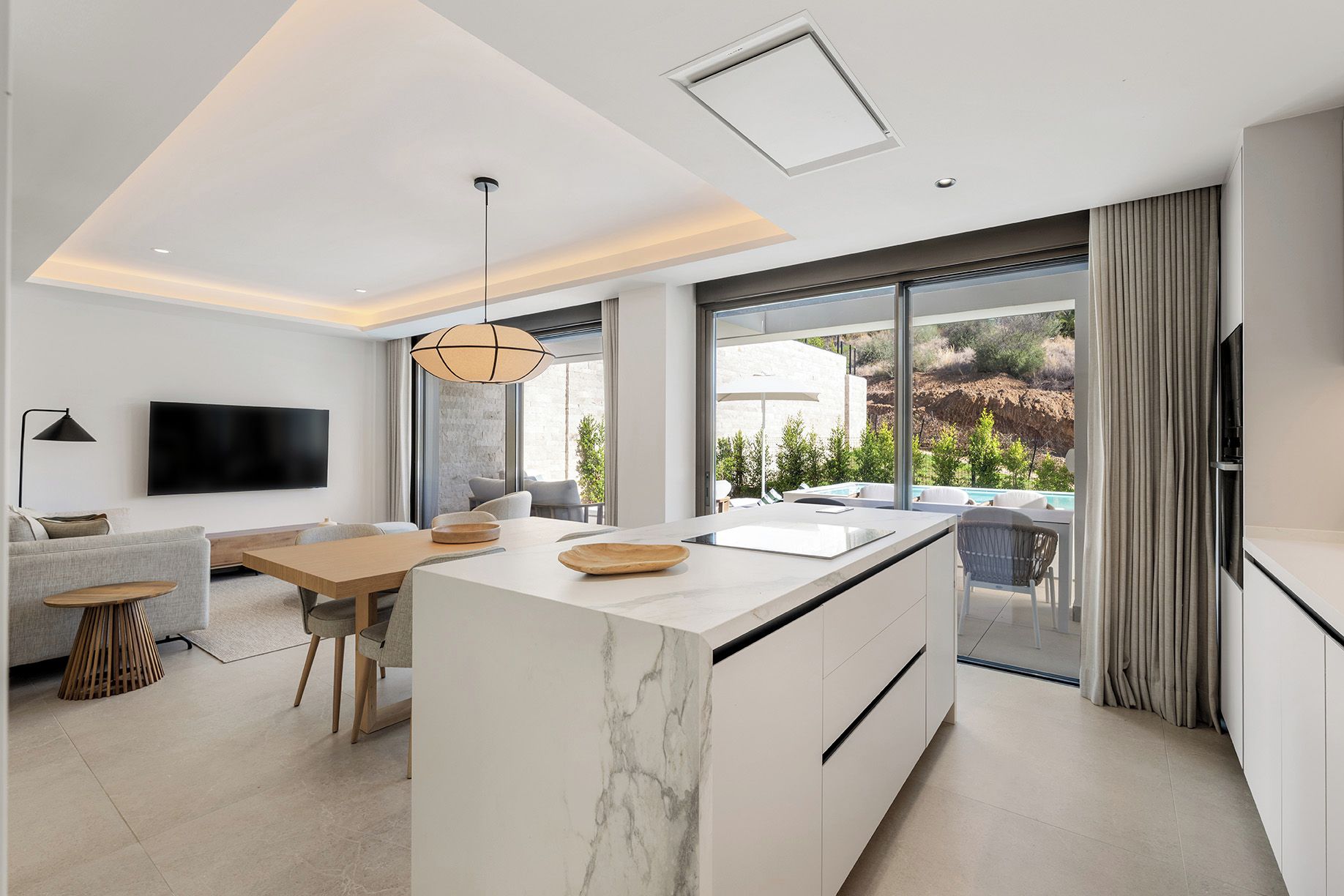 Een moderne keuken met een marmeren eiland, een eethoek met een houten tafel, en een groot raam met uitzicht op de omgeving.