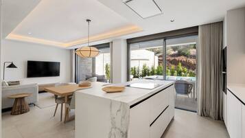 Een moderne keuken met een marmeren eiland, een eethoek met een houten tafel, en een groot raam met uitzicht op de omgeving.