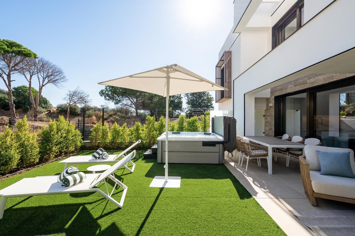 A modern outdoor living area with a hot tub, lounge chairs, and a dining table.