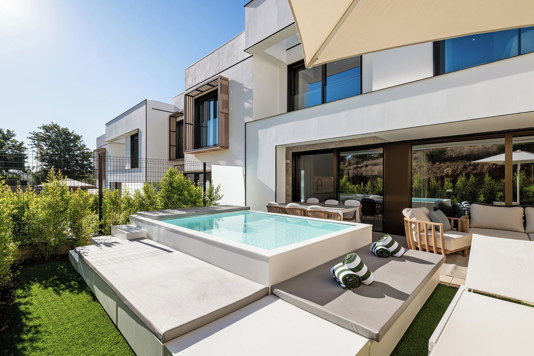 A modern outdoor pool area with a rectangular pool, lounge chairs, and a dining table.