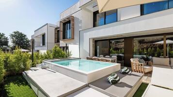 A modern outdoor pool area with a rectangular pool, lounge chairs, and a dining table.