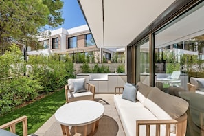 Un espace de vie extérieur moderne, aménagé avec un canapé, des fauteuils et une table ronde, le tout entouré de verdure et offrant une vue sur un bâtiment contemporain.