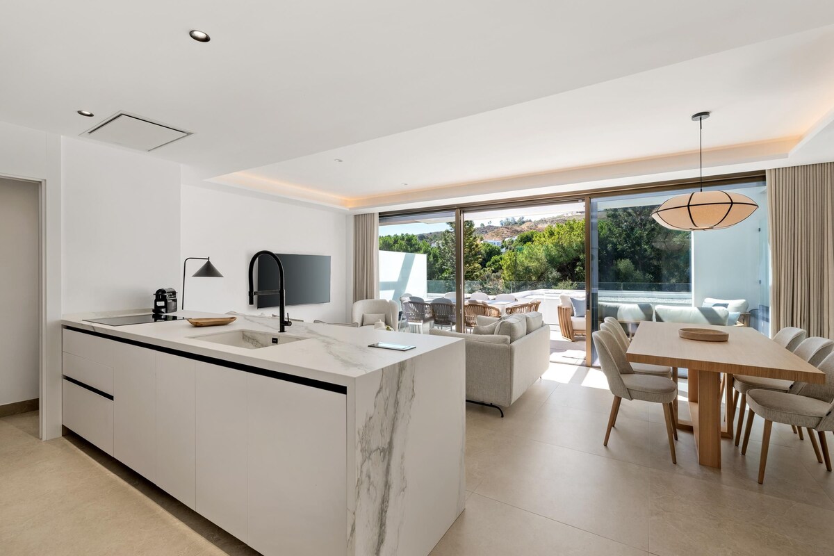 A modern kitchen with a marble island, a dining area with a table and chairs, and a large sliding glass door leading to an outdoor patio.
