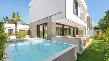 Een modern huis met een zwembad, tuinmeubilair buiten en een verzorgd gazon.