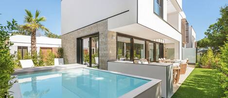 Una casa moderna con piscina, mobiliario exterior y un césped cuidado.