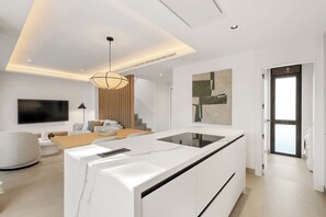 A modern kitchen with a central island, a dining area with a sofa and table, and a staircase leading to an upper level. - Wyndham Grand Residences La Cala Golf Mijas Costa (Mijas)