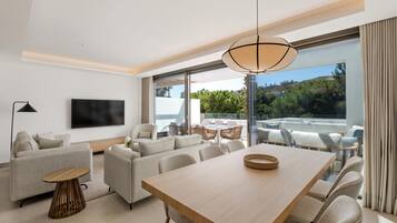 Een moderne woonkamer met een flatscreen televisie, een eethoek met een houten tafel en een balkon met zitplaatsen.