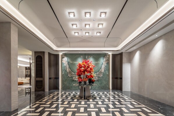 Un hall d’entrée moderne avec un sol à motifs géométriques, un arrangement floral central et un éclairage encastré au plafond.