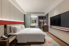 Une chambre d’hôtel avec un grand lit, une télévision, une armoire et une salle de bain visible à travers une porte ouverte.