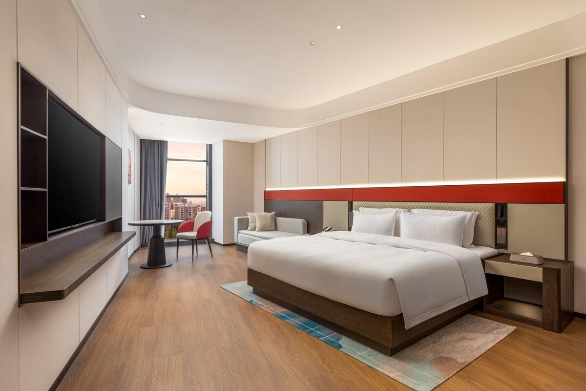 Une chambre d’hôtel moderne dotée d’un grand lit, d’une télévision à écran plat, d’un bureau et offrant une vue sur la ville.