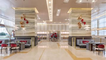 A spacious lobby with a central seating area, a decorative wall with hanging ornaments, and a modern ceiling design.