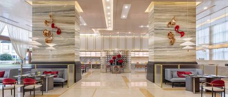 A spacious lobby with a central seating area, a decorative wall with hanging ornaments, and a modern ceiling design.