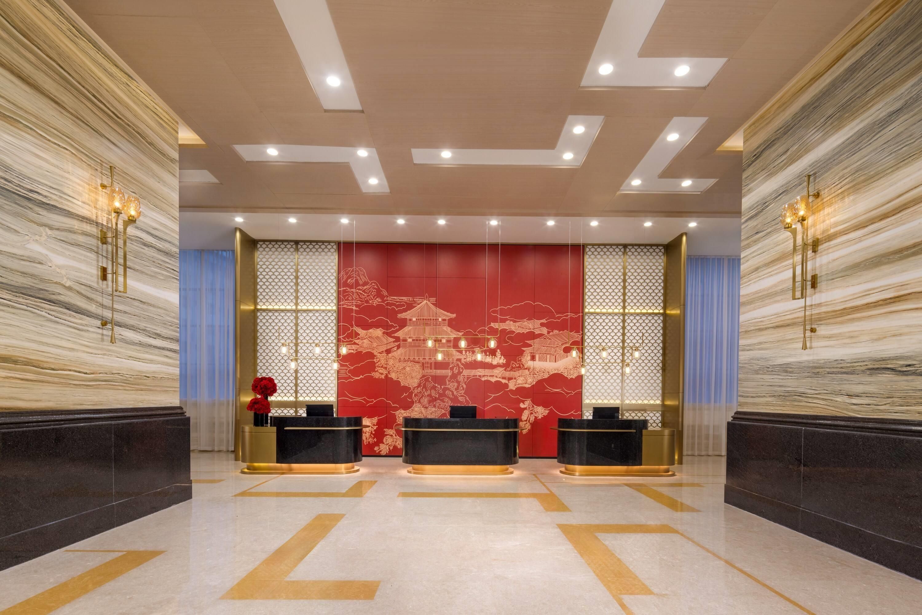 Un vestíbulo con mostrador de recepción, una pared decorativa roja y un piso con diseño.