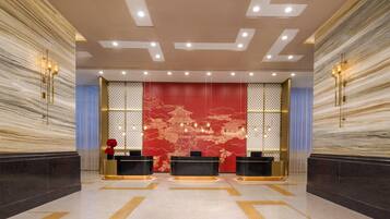 Un vestíbulo con mostrador de recepción, una pared decorativa roja y un piso con diseño.