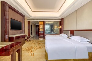 Habitación de hotel con una cama grande, televisión, escritorio y vistas a la ciudad a través de un ventanal.