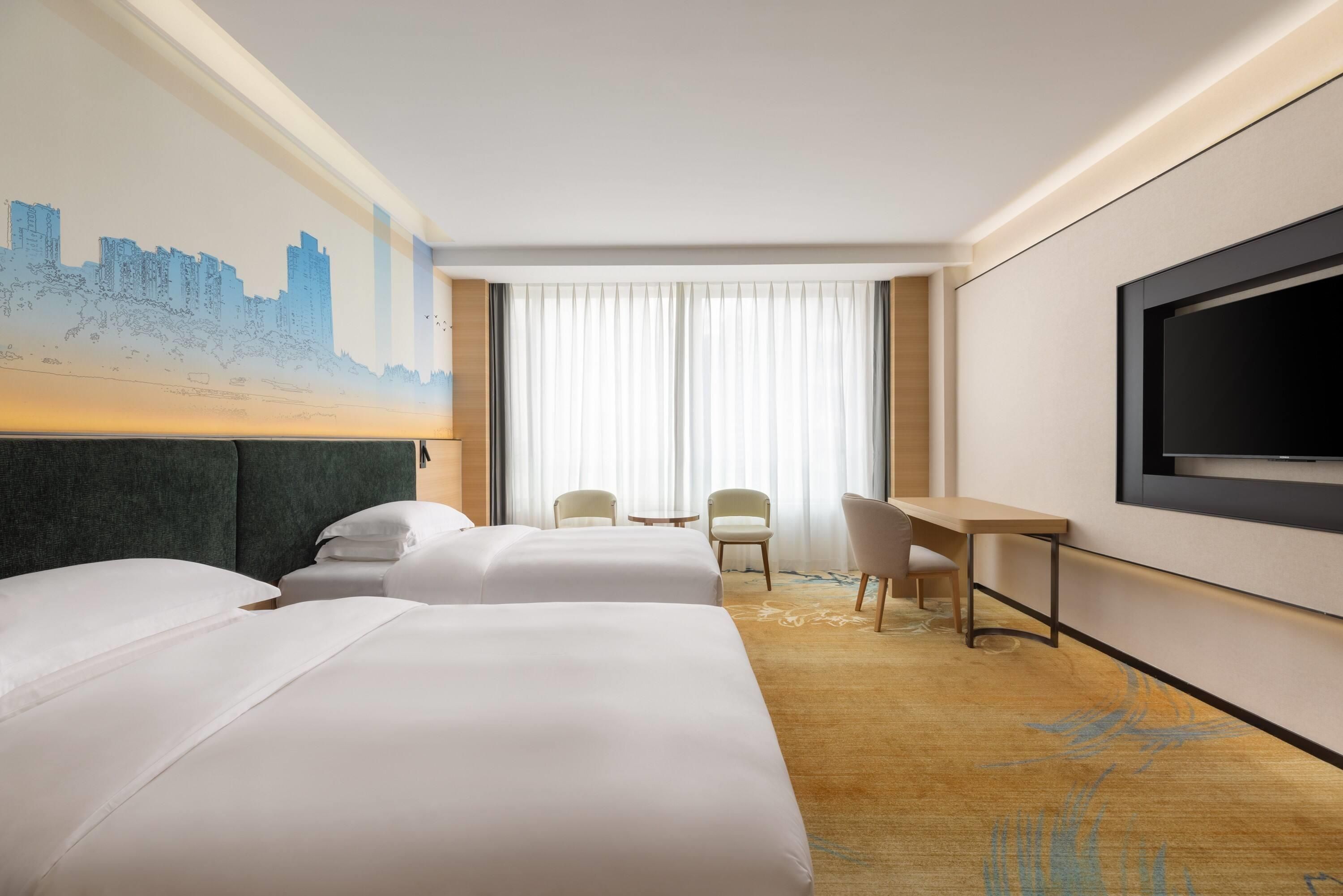 Une chambre d’hôtel avec deux lits, un bureau, une chaise, un téléviseur et une fresque murale représentant un paysage urbain.