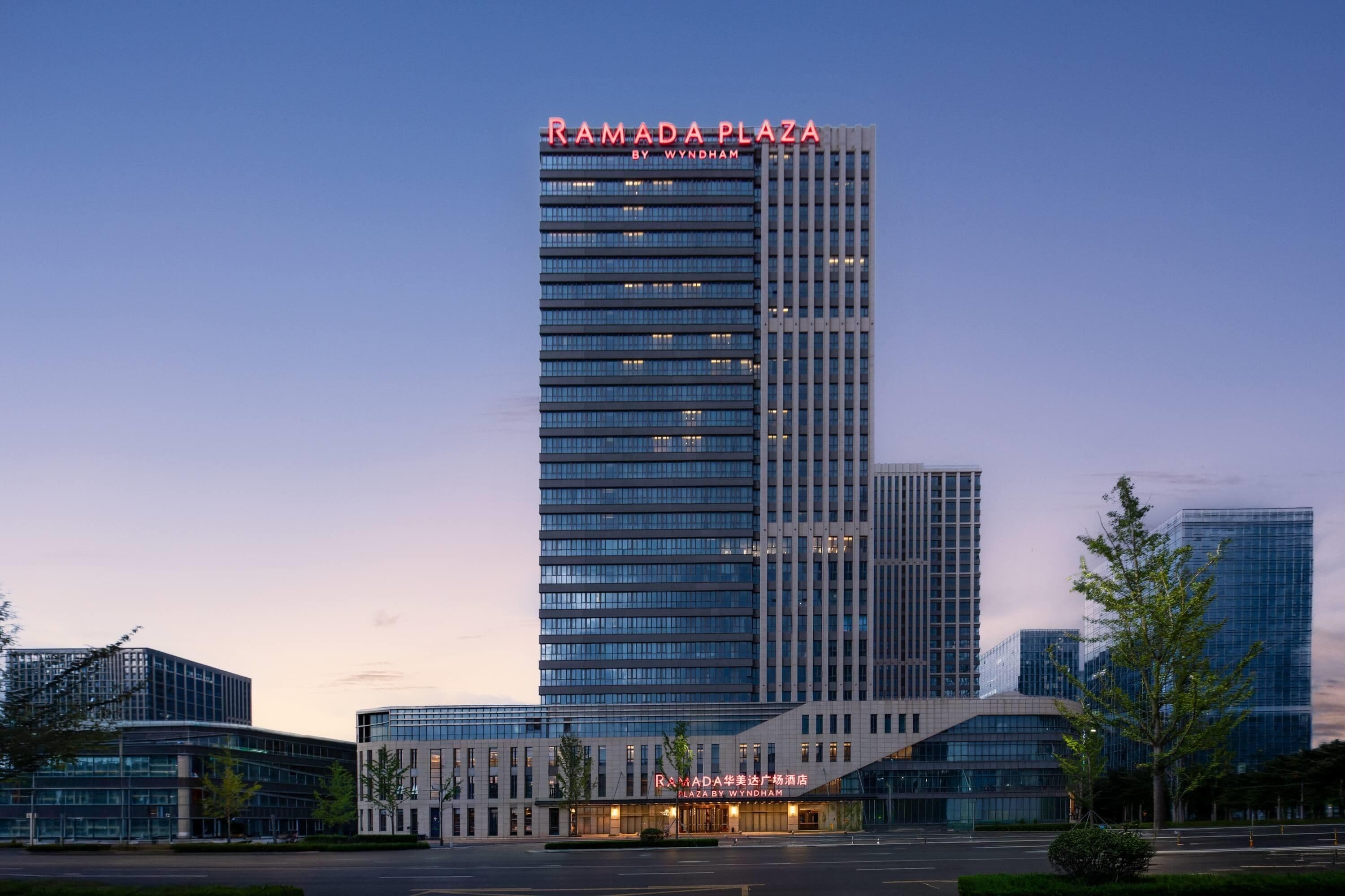Ein modernes Hochhaus-Hotel mit einem auffälligen 'RAMADA PLAZA BY WYNDHAM'-Schild an der Spitze.