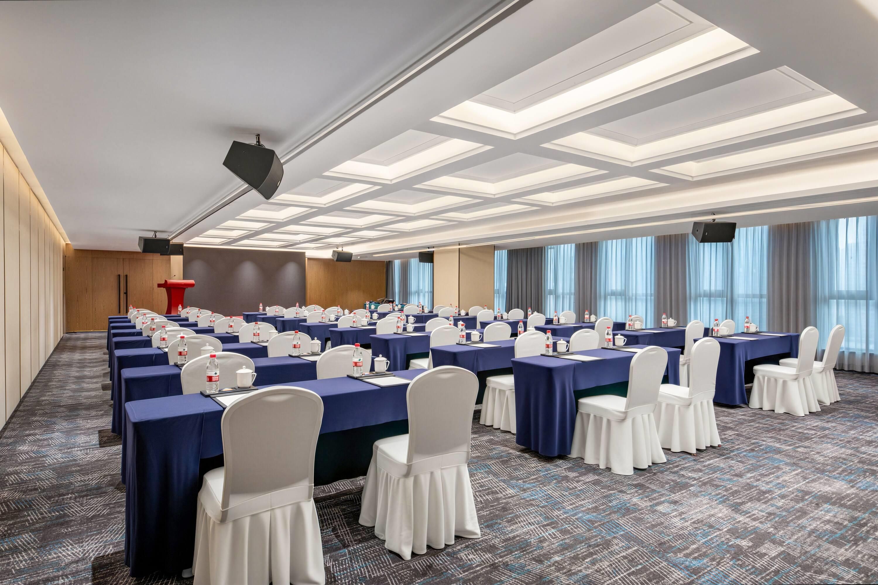 A conference room with multiple tables, chairs, and a stage area.