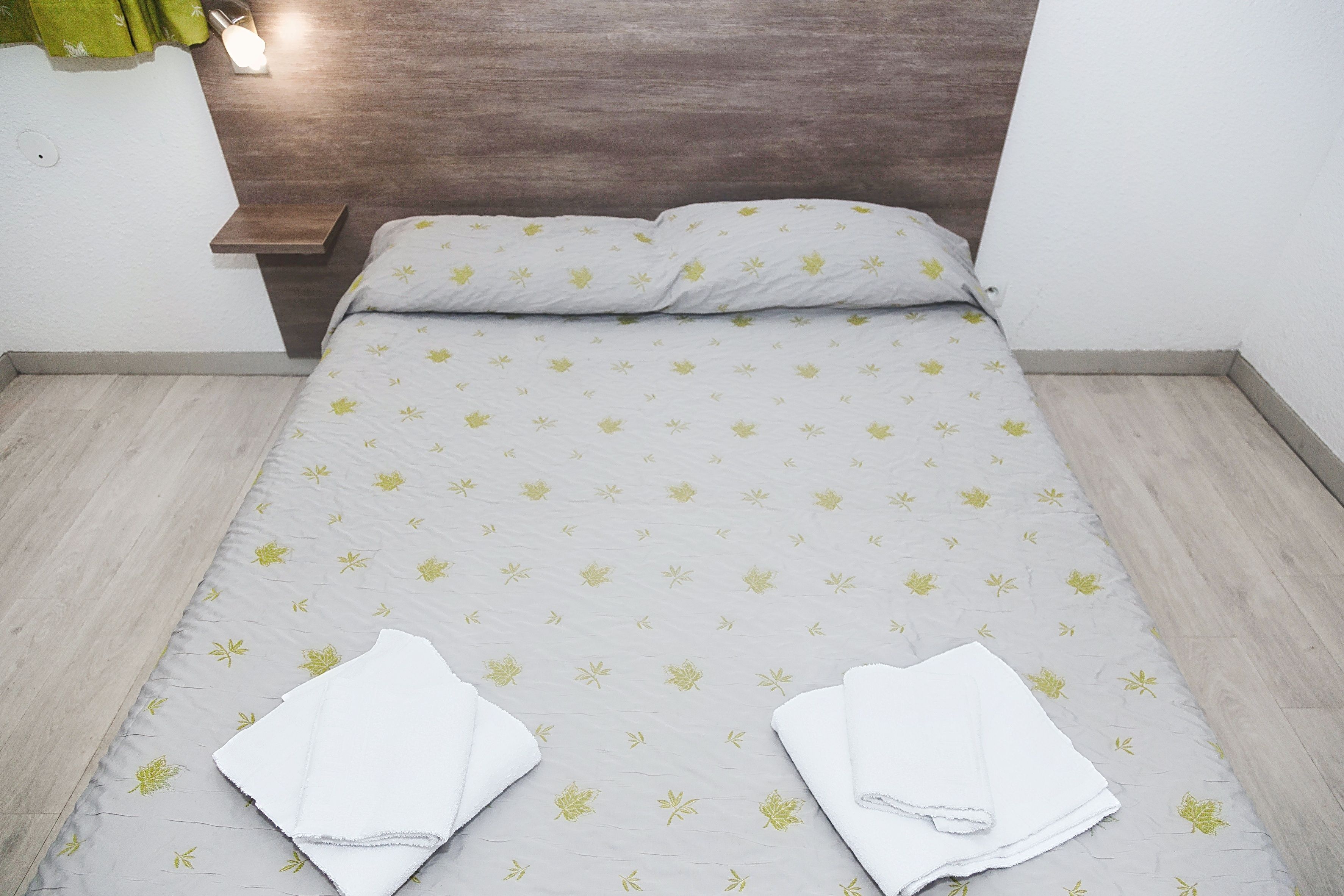 Een net opgemaakt bed met een bedspreide met patroon, twee witte handdoeken gevouwen, en een houten hoofdbord.