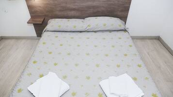 Een net opgemaakt bed met een bedspreide met patroon, twee witte handdoeken gevouwen, en een houten hoofdbord.