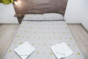 Una cama bien hecha con un edredón estampado, dos toallas blancas dobladas y un cabecero de madera.