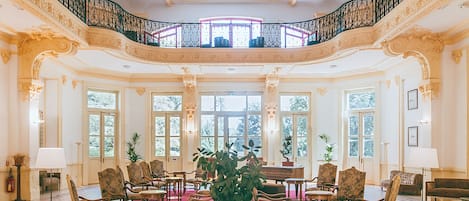 Un salón imponente con columnas ornamentadas, una alfombra roja y un candelabro.