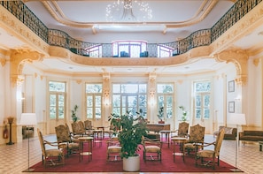Un salón imponente con columnas ornamentadas, una alfombra roja y un candelabro.