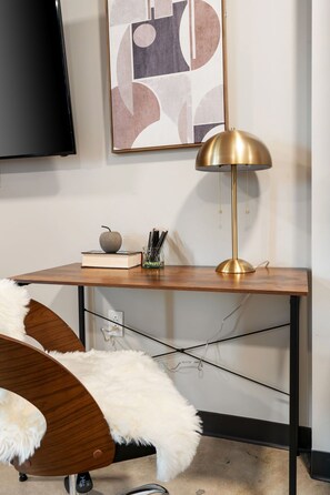 A modern room with a wooden desk, a gold lamp, a framed abstract artwork, and a fluffy white chair. - Chic Stay in the Heart of 5 Points Free Parking Walk to Food, Fun & Nightlife (Birmingham)