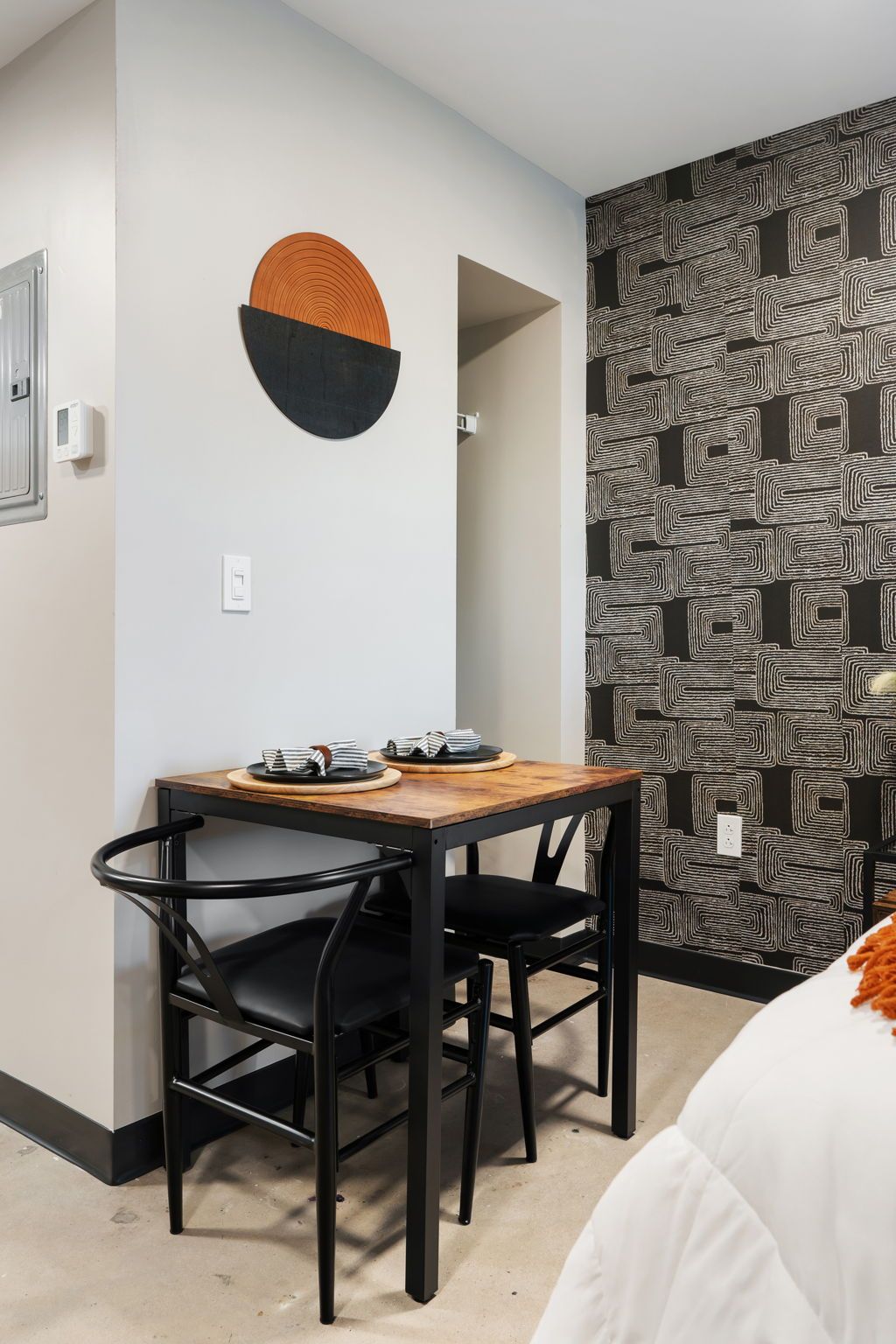 Un comedor con una mesa y sillas, una lámpara fijada en la pared y un papel tapiz estampado.