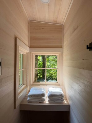 A narrow wooden room with a window, a towel rack, and a light fixture.