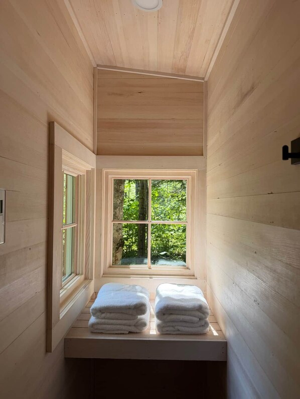 A narrow wooden room with a window, a towel rack, and a light fixture.