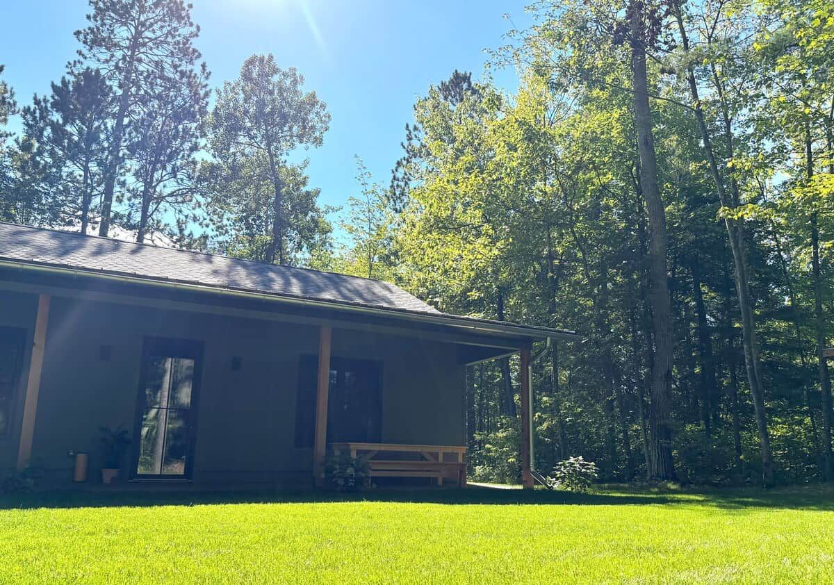 A single-story building with a porch, surrounded by a well-maintained lawn and tall trees.