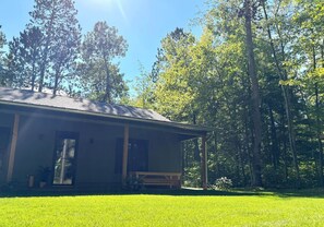A single-story building with a porch, surrounded by a well-maintained lawn and tall trees.