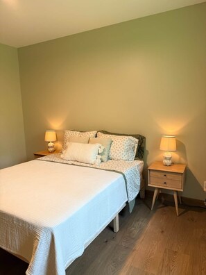 A bedroom with a bed, two bedside tables with lamps, and a wooden floor.