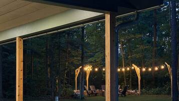 Une terrasse extérieure couverte, avec des poutres en bois, un sol en béton et des guirlandes lumineuses.