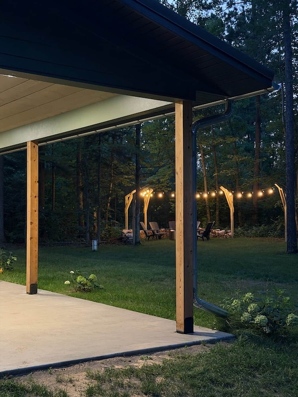 Un patio exterior cubierto con vigas de madera, piso de concreto y luces colgantes.