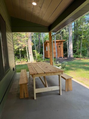 Een houten picknicktafel met banken onder een overdekte veranda, met uitzicht op een bos.