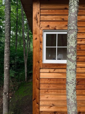A wooden cabin with a window, surrounded by trees.