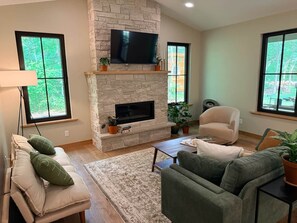 Una sala de estar con chimenea de piedra, televisor de pantalla plana, sofá, sillón y mesa de centro.