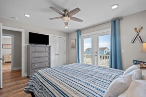 A bedroom with a bed, a ceiling fan, a dresser, a television, and a view of the outside. - Ocean Views with Heated Pool! One Row from Beach! (Oak Island)
