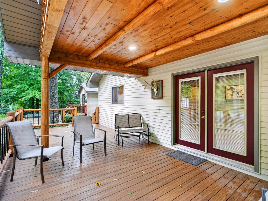 A covered wooden deck with chairs, a bench, and a door with glass panels.