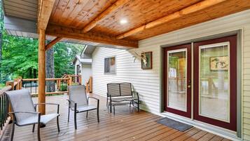 A covered wooden deck with chairs, a bench, and a door with glass panels.