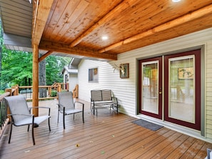 A covered wooden deck with chairs, a bench, and a door with glass panels.
