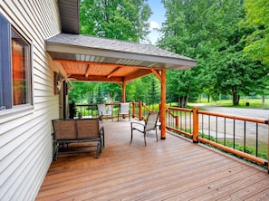 A wooden deck with outdoor furniture, a covered area, and a view of a forested area. - Escape to Buck Fever Lodge! An Exclusive Trophy Whitetail Ranch Experience! (Gladwin)