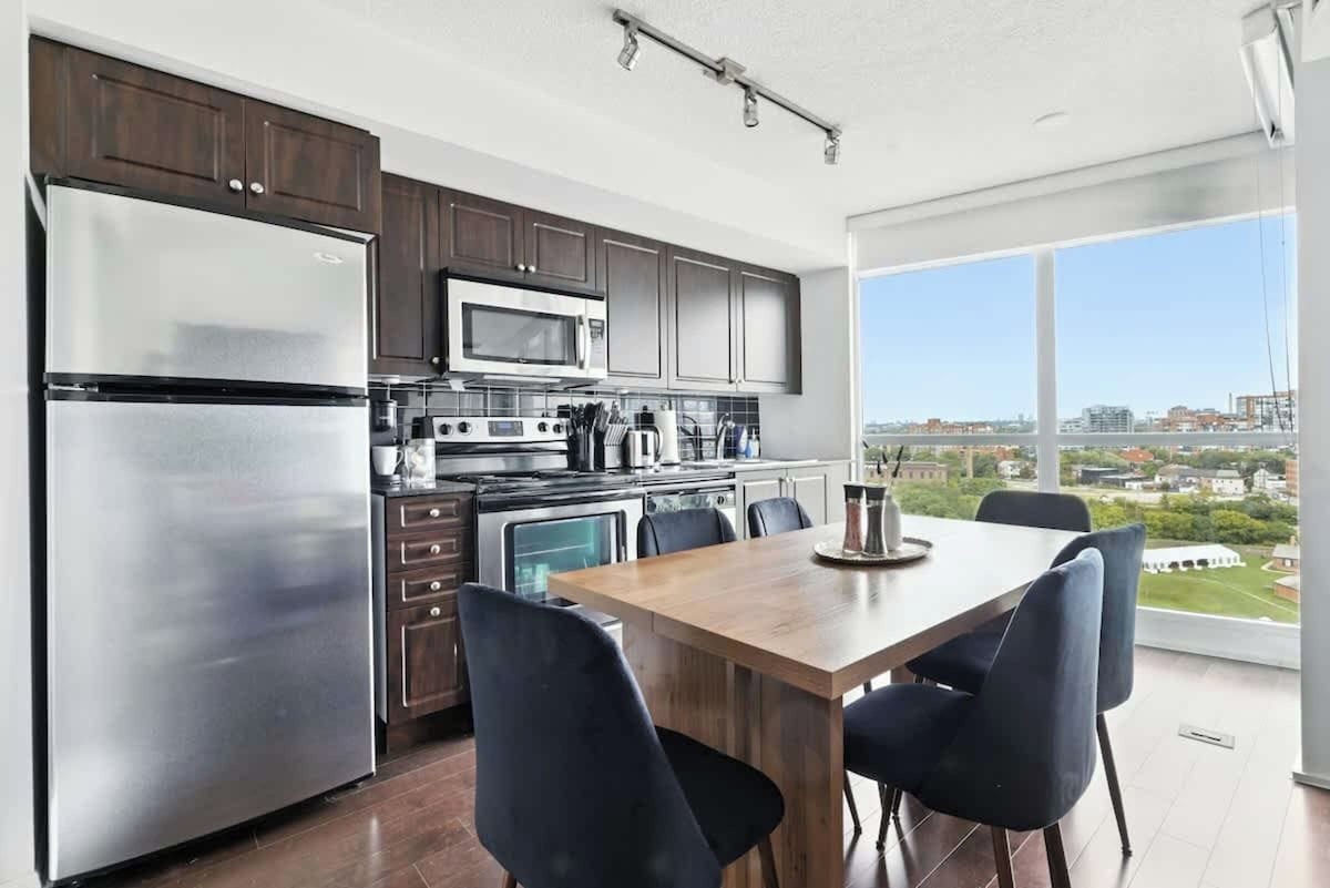 Eine moderne Küche mit Edelstahlgeräten, ein Essbereich mit Holztisch und -stühlen sowie ein großes Fenster mit Blick auf die Stadt.