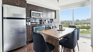 Uma cozinha moderna com eletrodomésticos de aço inoxidável, uma área de jantar com mesa e cadeiras de madeira, e uma janela grande com vista para a cidade.