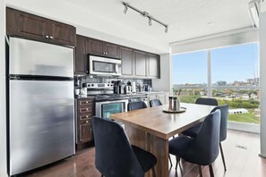 Eine moderne Küche mit Edelstahlgeräten, ein Essbereich mit Holztisch und -stühlen sowie ein großes Fenster mit Blick auf die Stadt.