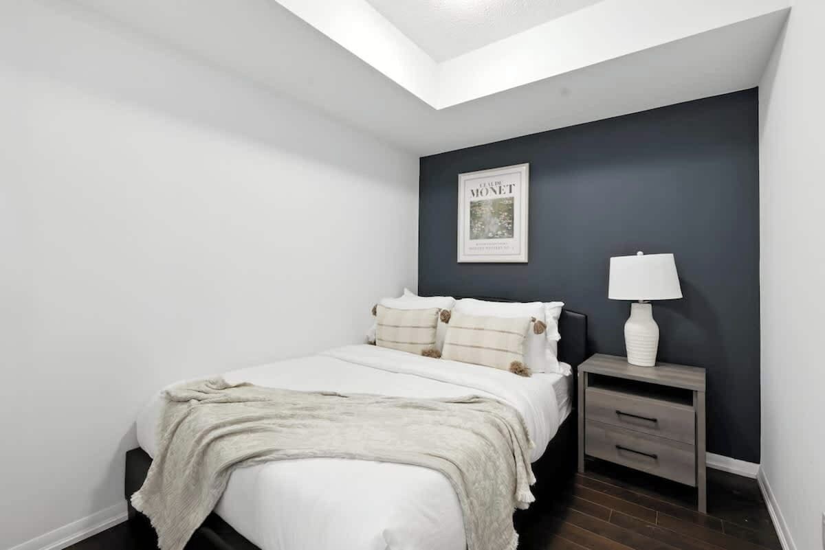 A bedroom with a bed, a nightstand, a lamp, and a framed picture on the wall.